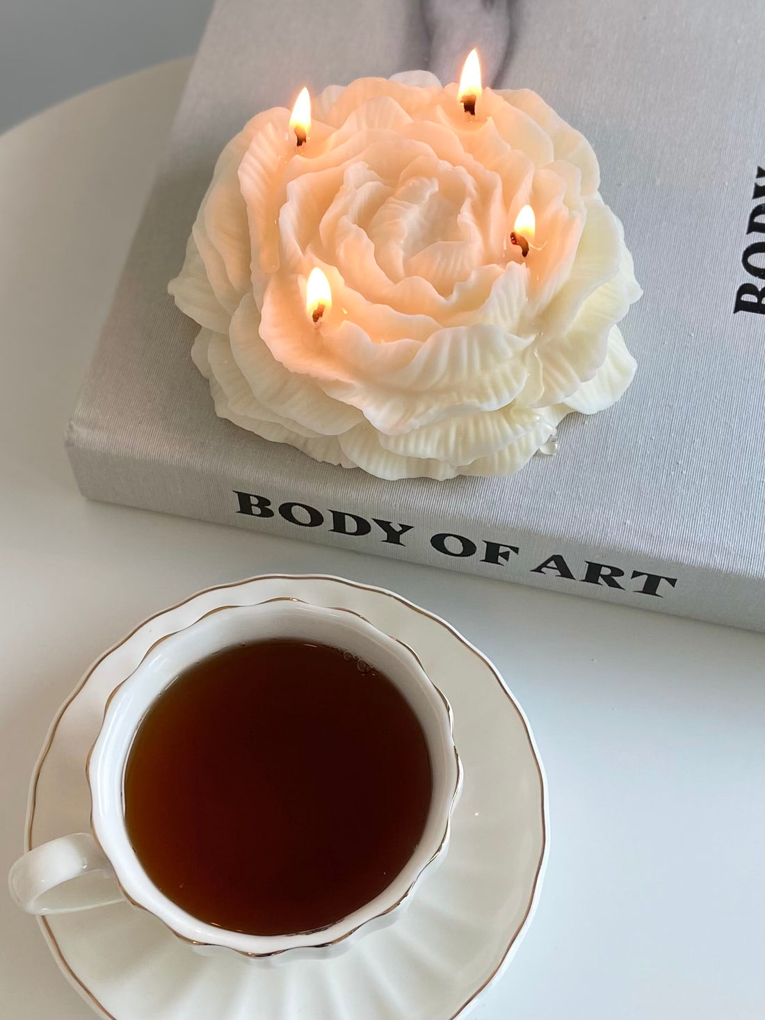 large peony shaped candle with a cup of coffee on a "body of art" book